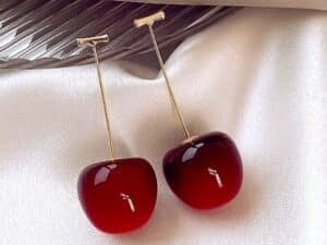 “Trendy cherry drop earrings with red fruit charm and gold-tone stem worn on ear”