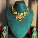 “Gold-plated temple green stone necklace set displayed on jewellery stand with matching earrings – traditional Indian wedding jewellery.”
