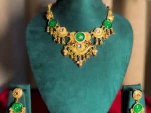 “Gold-plated temple green stone necklace set displayed on jewellery stand with matching earrings – traditional Indian wedding jewellery.”