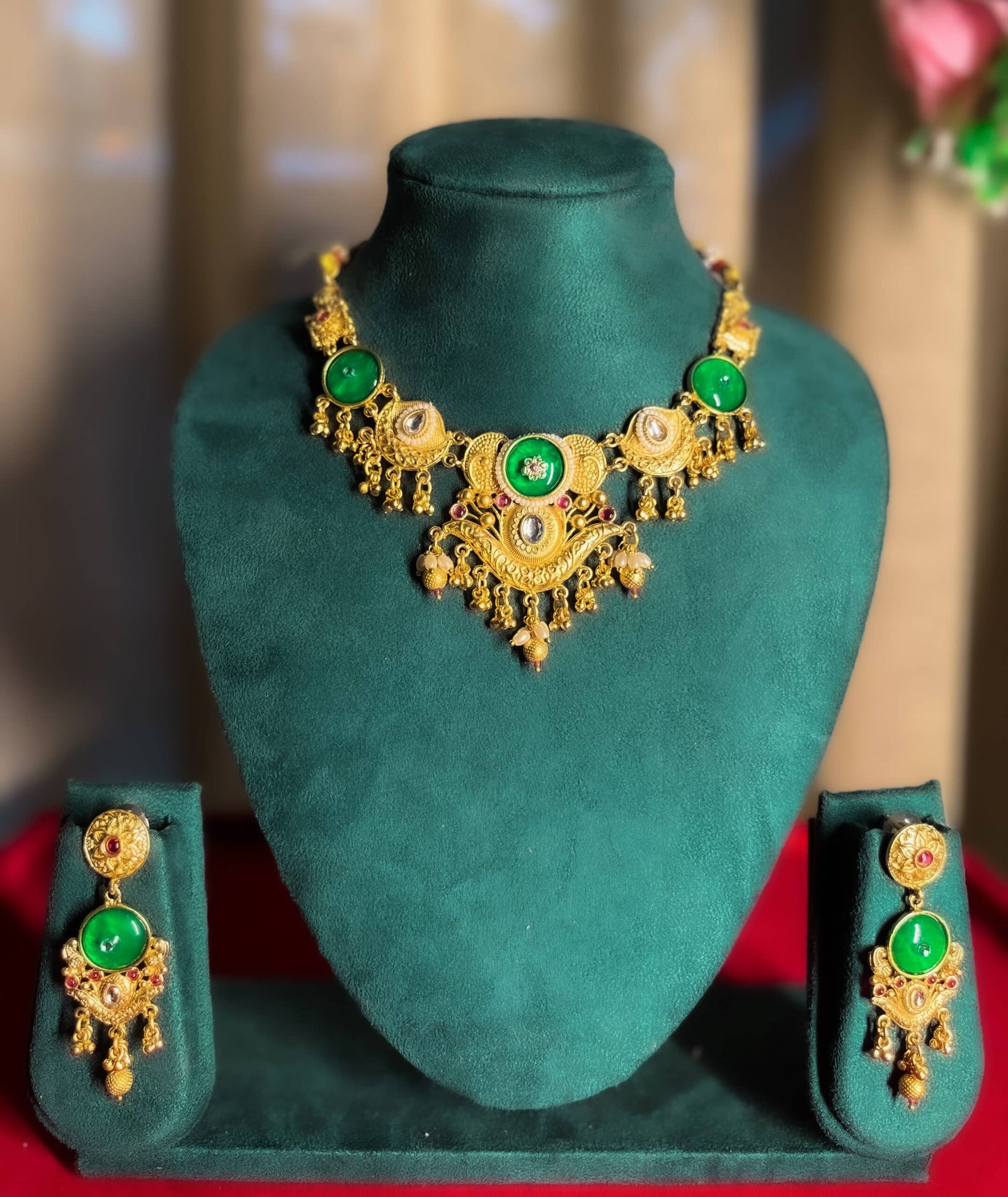 “Gold-plated temple green stone necklace set displayed on jewellery stand with matching earrings – traditional Indian wedding jewellery.”